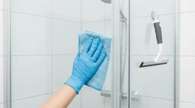 Mano con guanto blu pulisce il vetro della doccia con un panno in microfibra